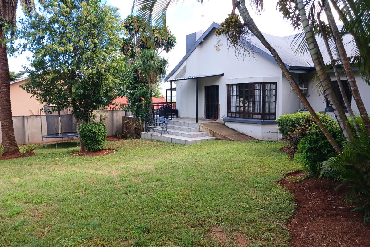 Rear view of the house featuring a lawn, a small tiled patio with steps, and a bay window.