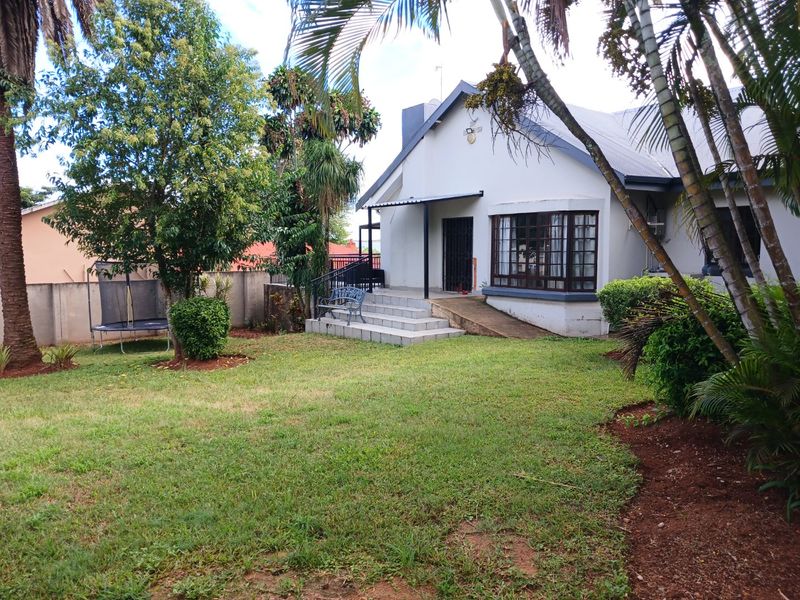 Rear view of the house featuring a lawn, a small tiled patio with steps, and a bay window.