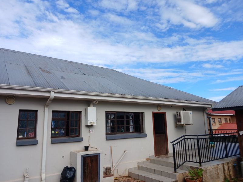 Rear exterior view of the property featuring a corrugated metal roof, gas geyser, air conditioning unit, and concrete steps leading to a side entrance.