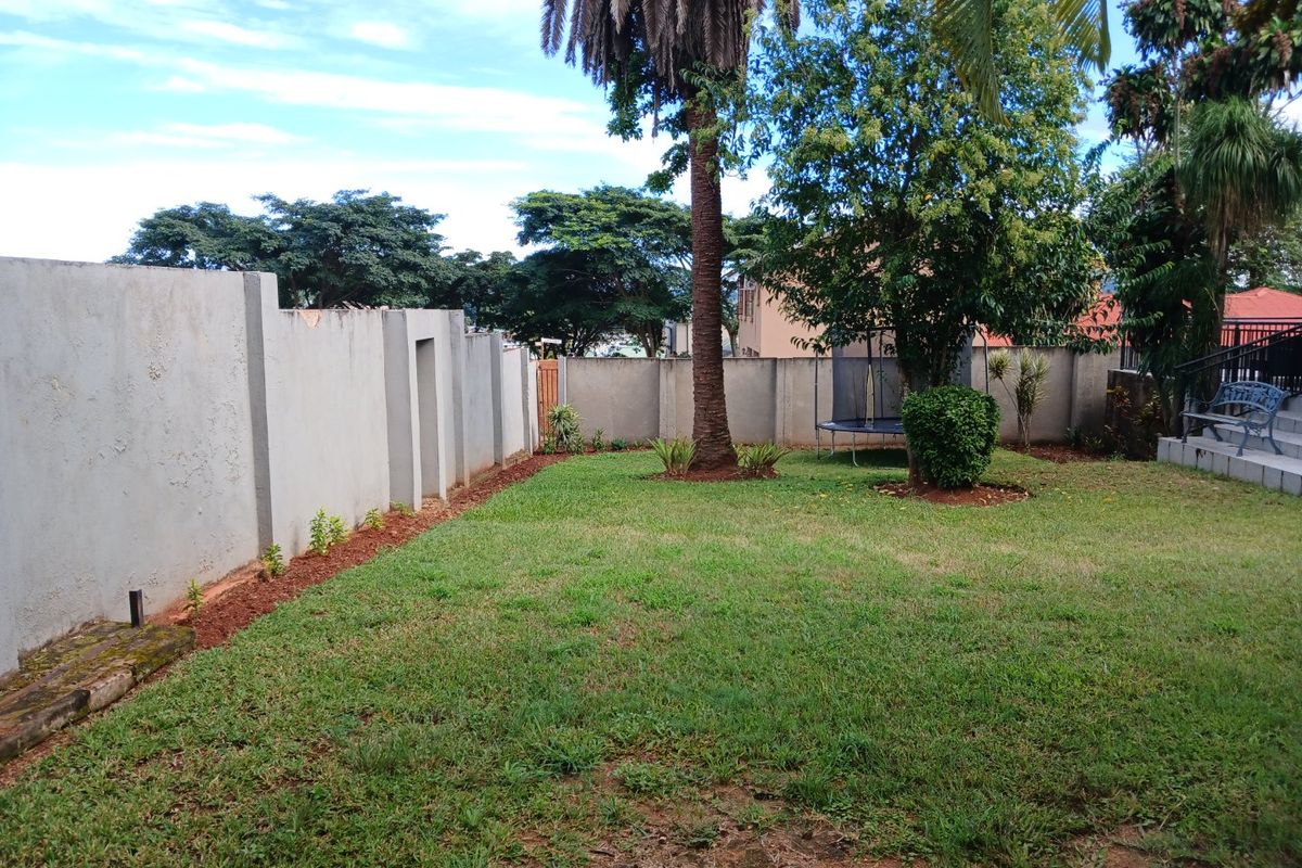 A spacious private garden featuring a well-established lawn, mature palm tree, and high perimeter boundary walls providing privacy.