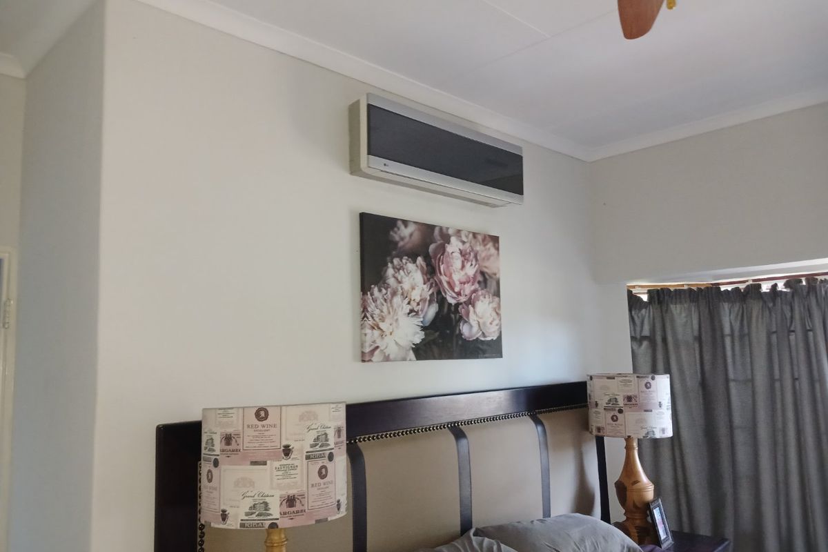 A comfortable bedroom featuring a wall-mounted air conditioning unit and a ceiling fan, providing climate control and ventilation.