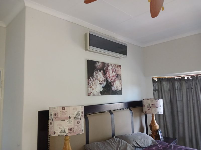A comfortable bedroom featuring a wall-mounted air conditioning unit and a ceiling fan, providing climate control and ventilation.