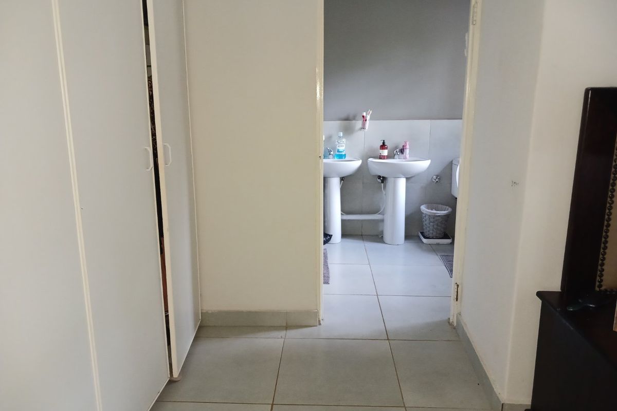A view through a doorway into a bathroom featuring dual pedestal wash basins and tiled flooring, with adjacent built-in cupboard storage.