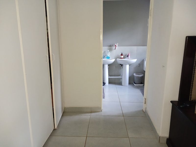 A view through a doorway into a bathroom featuring dual pedestal wash basins and tiled flooring, with adjacent built-in cupboard storage.