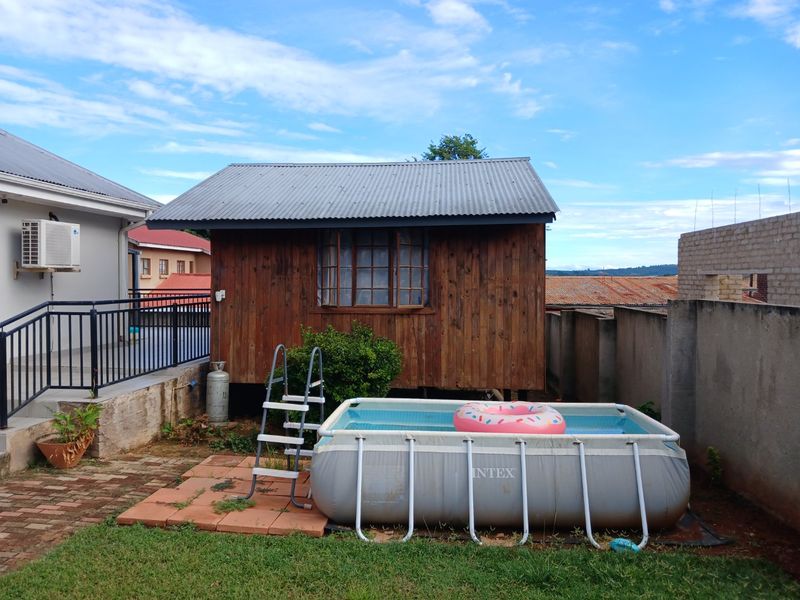 Rear garden area featuring a timber cabin with a corrugated metal roof, adjacent to a paved section and a portable above-ground pool.