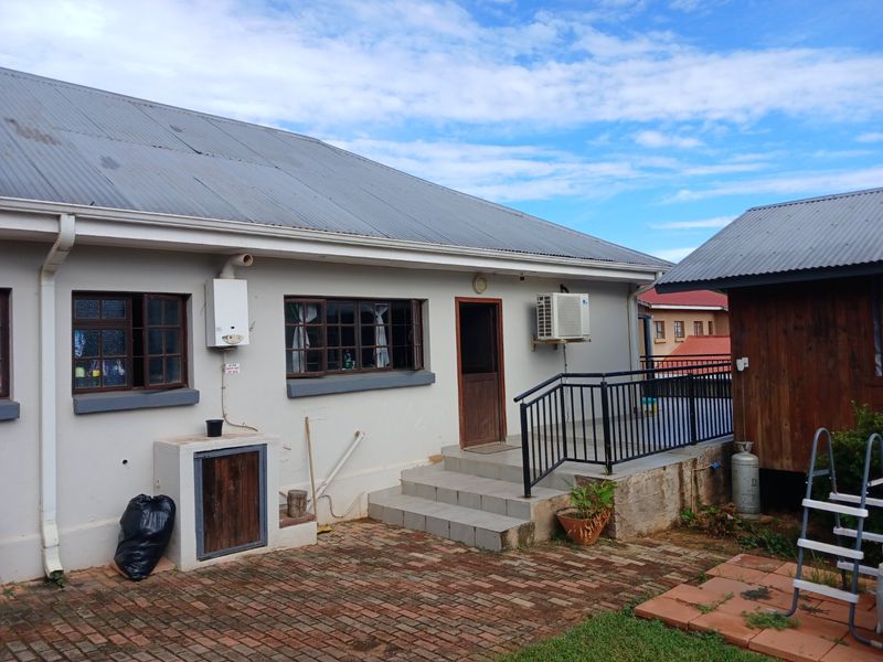 Rear view of the property featuring a paved patio area, tiled steps with metal railing, gas geyser, and air conditioning unit.