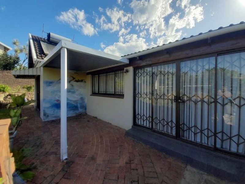 A covered brick-paved patio area featuring sliding glass doors with security gates and a solar water heating system on the roof.