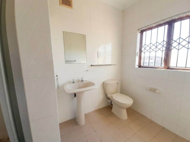 A functional bathroom featuring a pedestal basin, toilet, and tiled walls, equipped with security bars on the window for added safety.