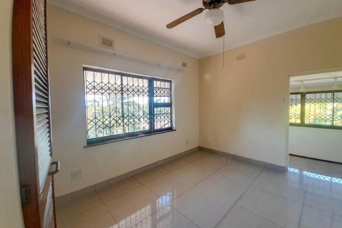 A bright, empty bedroom featuring tiled flooring, a ceiling fan, and security bars on the windows, offering a clean canvas for personalization.