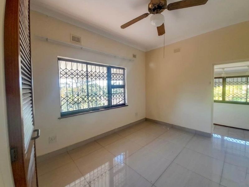 A bright, empty bedroom featuring tiled flooring, a ceiling fan, and security bars on the windows, offering a clean canvas for personalization.