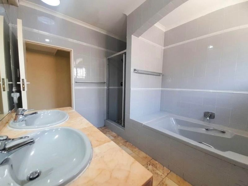 A spacious bathroom featuring a double vanity, a built-in bathtub, and a separate shower enclosure with neutral wall tiling.