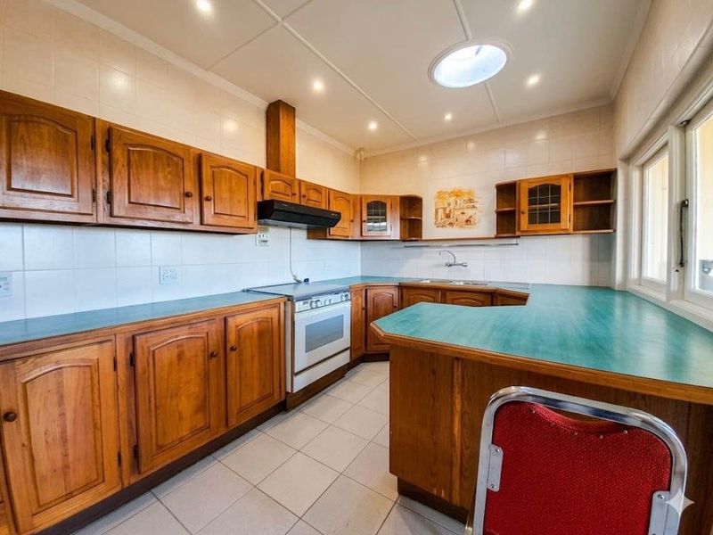 A functional kitchen featuring wooden cabinetry, laminate countertops, a freestanding oven with extractor fan, and a skylight providing natural light.