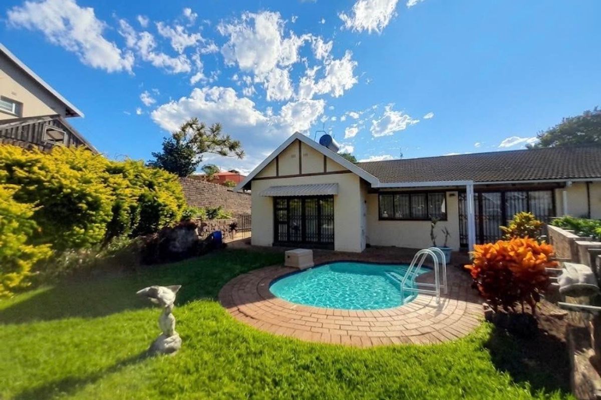 A well-maintained rear garden area featuring a compact swimming pool with brick paving, surrounded by established landscaping and a residential building facade.