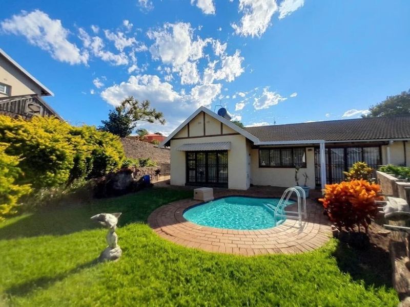 A well-maintained rear garden area featuring a compact swimming pool with brick paving, surrounded by established landscaping and a residential building facade.