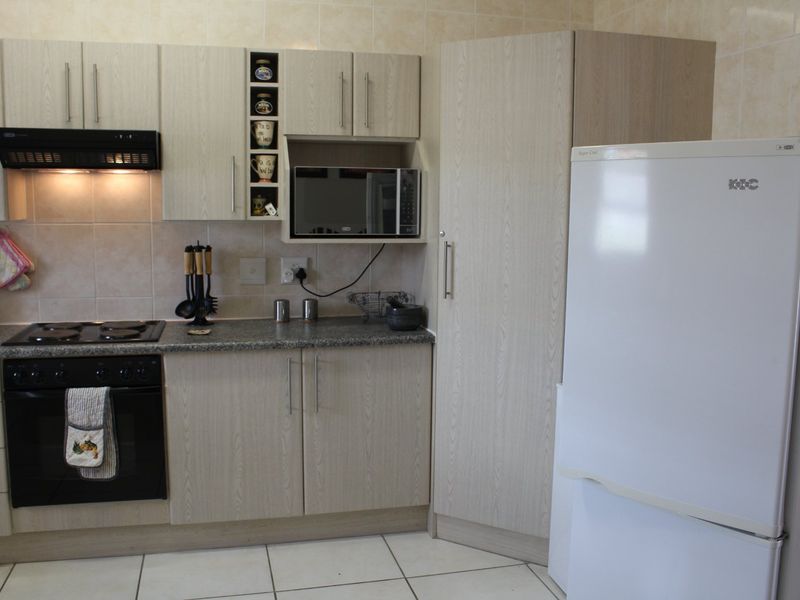 A functional kitchen featuring light wood-grain cabinetry, granite countertops, a built-in oven and hob, and tiled finishes throughout.