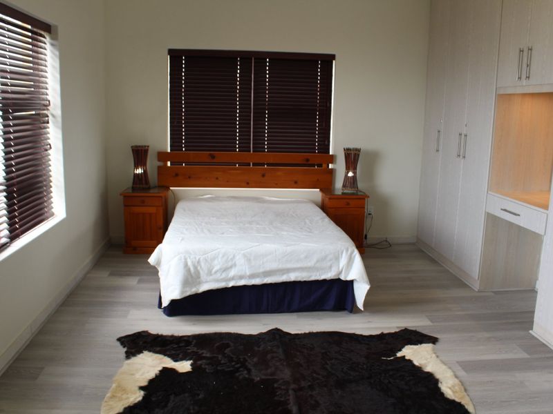 A well-maintained bedroom featuring light-toned laminate flooring, ample built-in cupboard space, a dedicated vanity area, and dark venetian blinds for privacy.