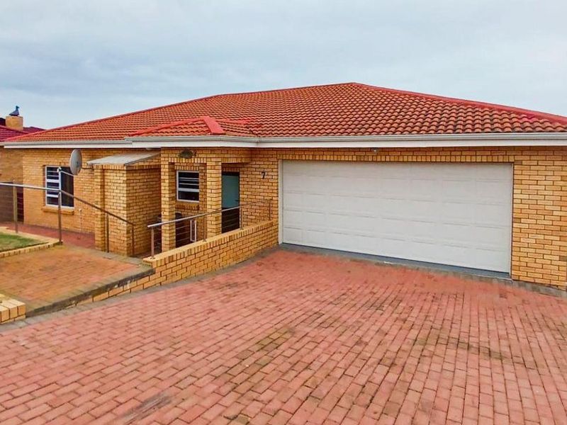 Front view of a brick house featuring a paved driveway, double garage, and tiled roof, situated in a residential area.