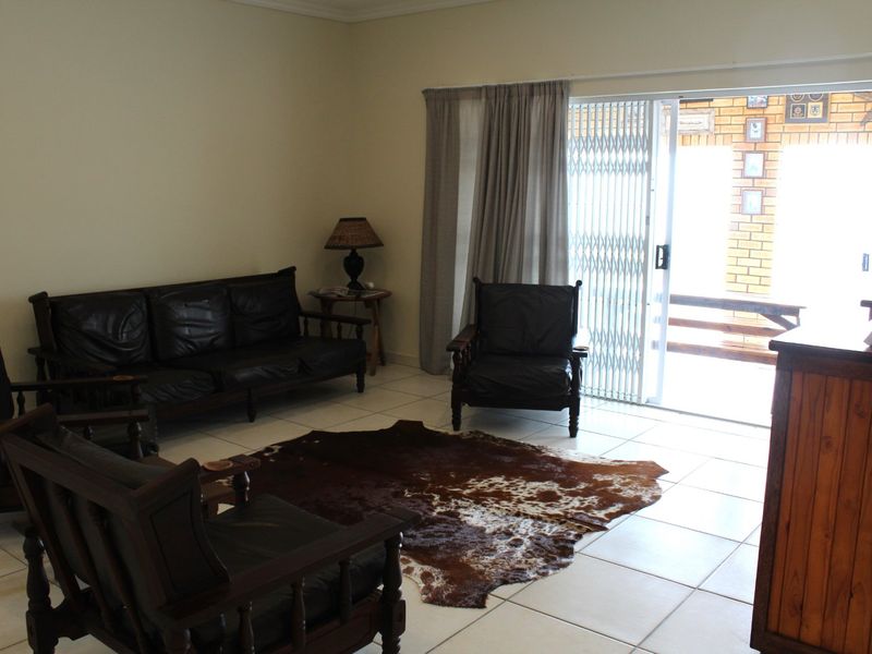 A living room featuring tiled flooring and a sliding glass door with a security gate, providing direct access to the outdoor area.
