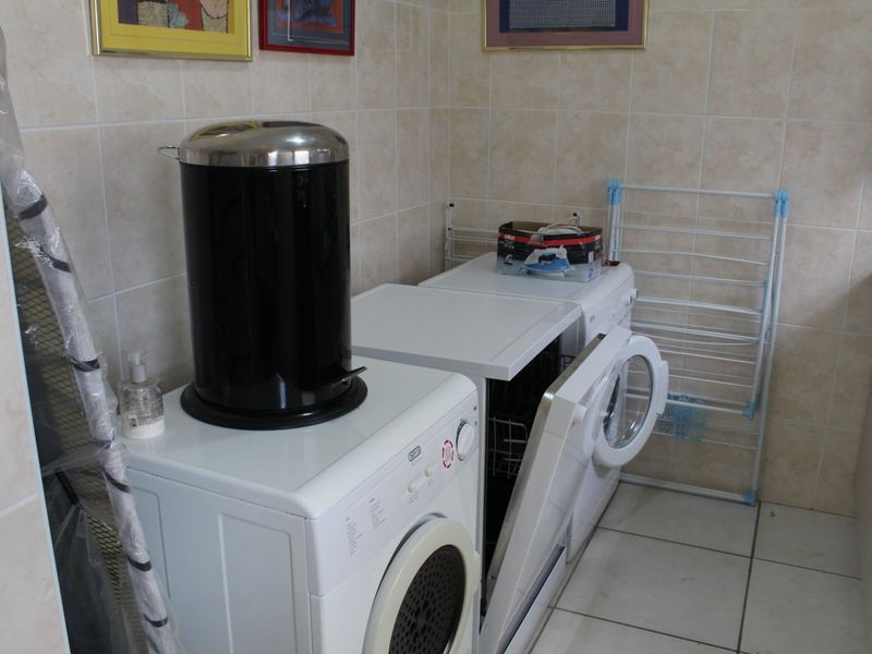 A functional laundry room featuring tiled walls and flooring with space for multiple appliances and built-in cabinetry.