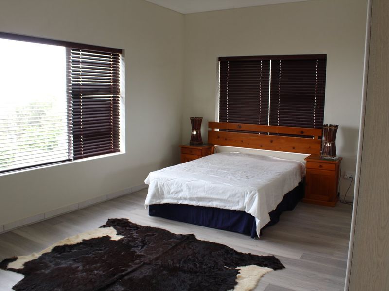 A well-lit bedroom featuring neutral walls, laminate flooring, and dark venetian blinds, offering a clean and functional living space.