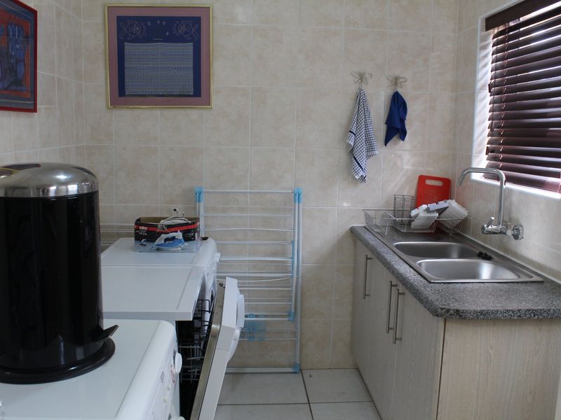 Functional laundry room featuring a double stainless steel sink, laminate cabinetry, granite-look countertops, and full-height ceramic wall tiling.