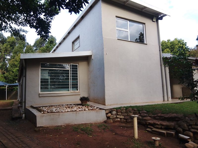 Rear view of the house featuring a two-story structure with aluminium windows, security bars, and a raised garden bed with stone retaining wall.