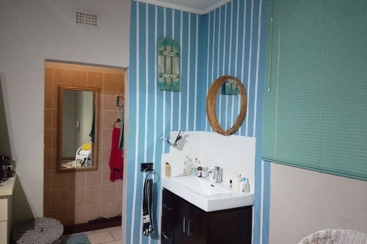 A bathroom featuring a vanity cabinet with a basin, tiled splashback, and a roller blind, with an adjacent tiled area visible through the doorway.