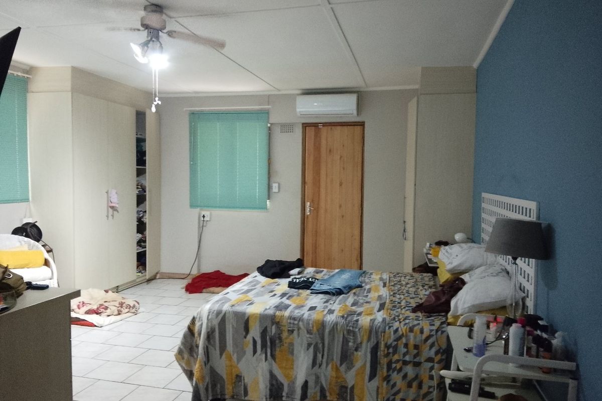 Spacious bedroom featuring built-in cupboards, tiled flooring, a ceiling fan, and a wall-mounted air conditioning unit.