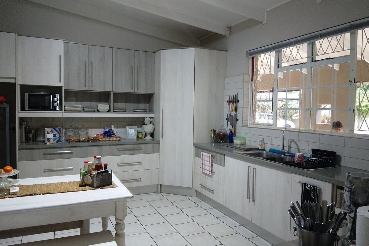 A functional kitchen featuring light-toned cabinetry, subway tile backsplash, tiled flooring, and a double sink with ample counter space.