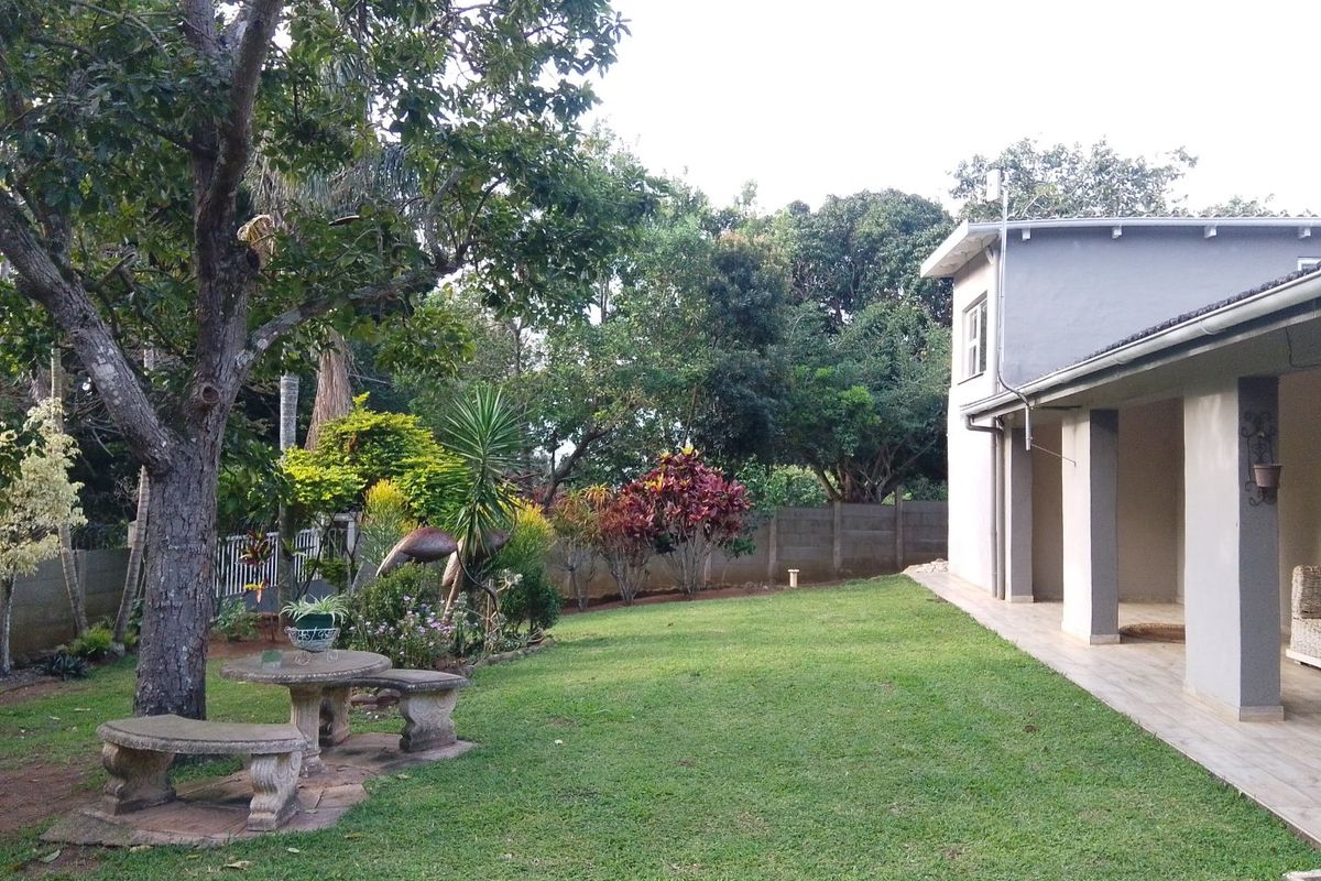 A well-maintained rear garden featuring a spacious lawn, mature trees, and a covered patio area with tiled flooring.