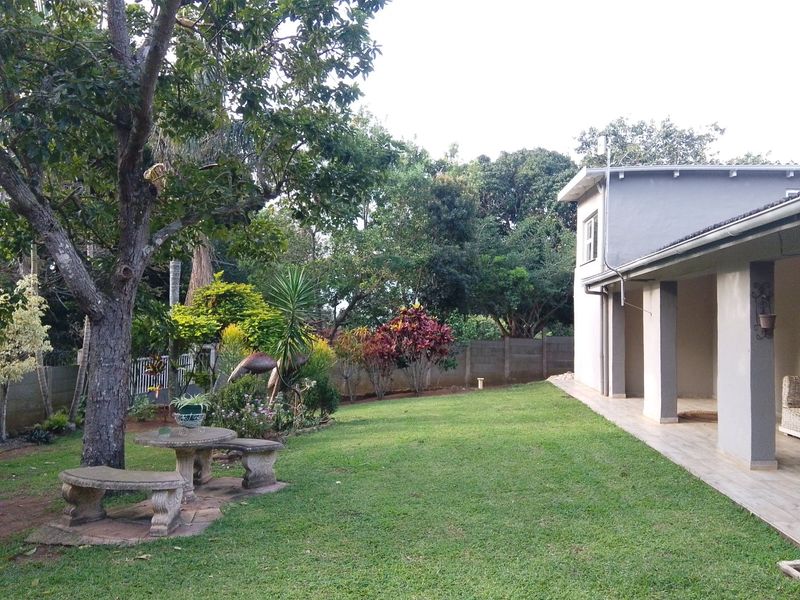 A well-maintained rear garden featuring a spacious lawn, mature trees, and a covered patio area with tiled flooring.