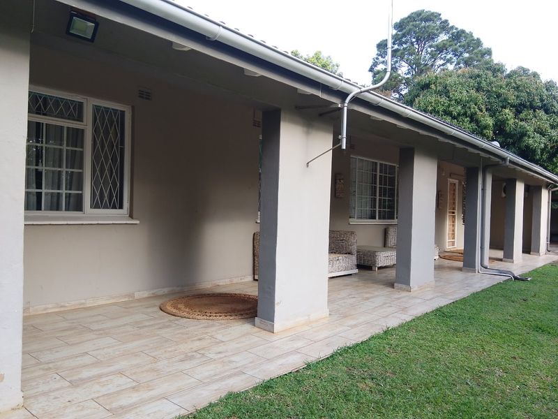 A covered patio area featuring tiled flooring, concrete support pillars, and security-barred windows, overlooking the garden.