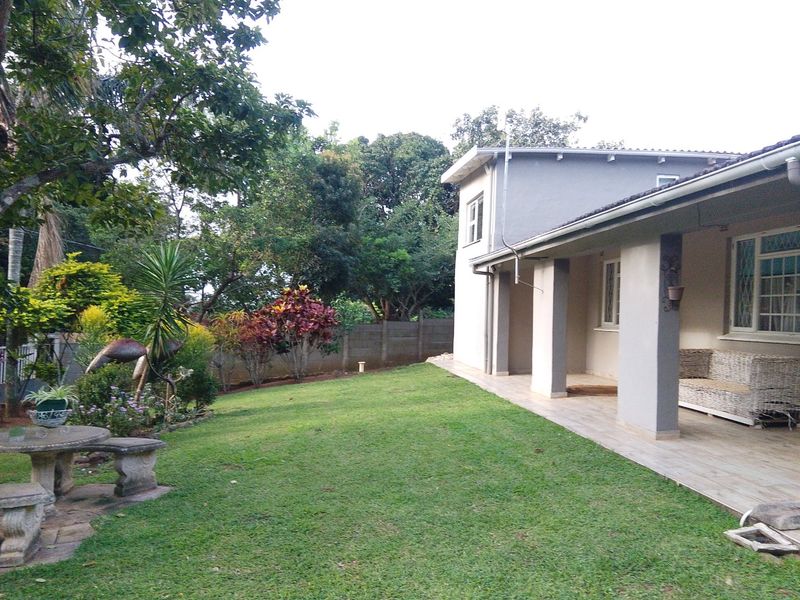A well-maintained rear exterior view featuring a covered patio with tiled flooring, concrete pillars, and a spacious landscaped garden with a boundary wall.