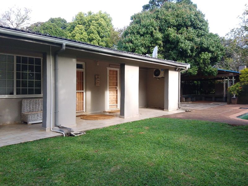 Rear view of the house featuring a covered tiled patio, lawn area, and exterior wall-mounted air conditioning unit.