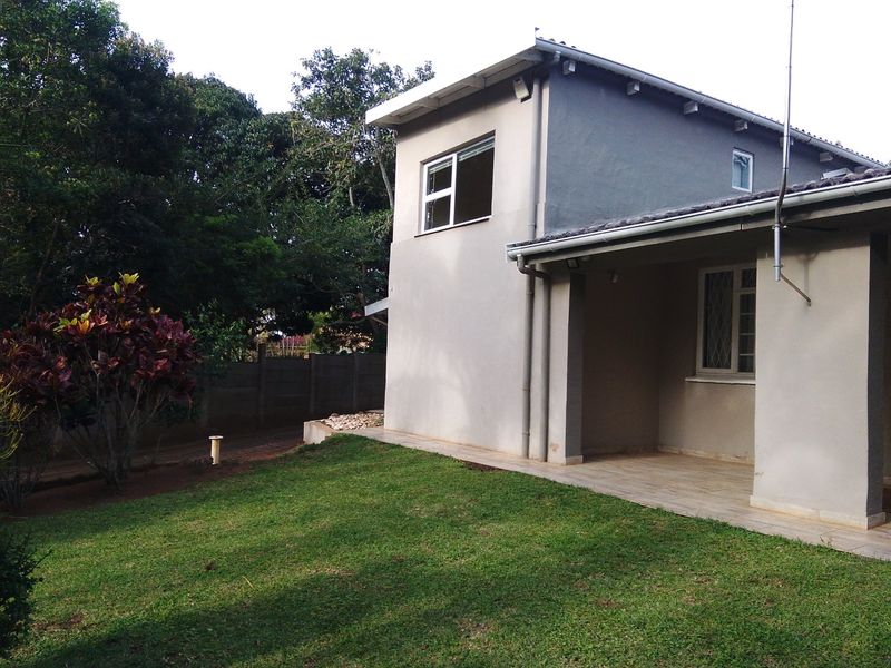 Rear view of the property featuring a covered tiled patio, landscaped garden, and concrete boundary wall.