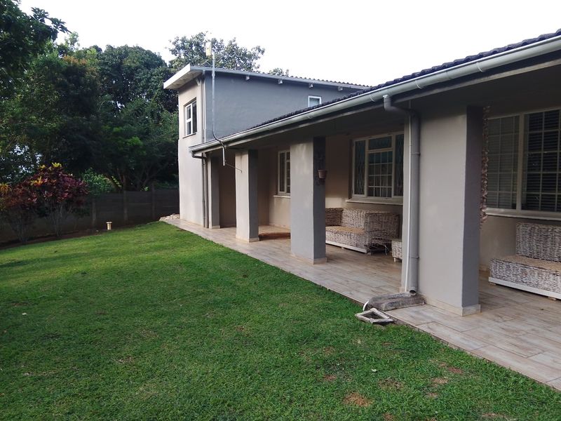 Rear view of the house featuring a covered tiled patio, concrete pillars, and a well-maintained lawn area.
