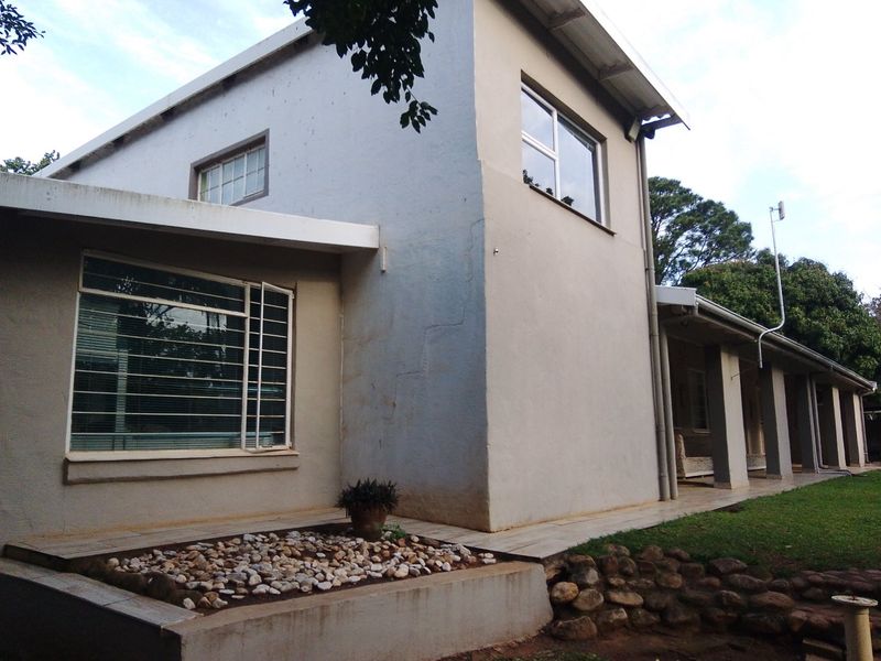 Rear view of the house featuring a covered patio, stone retaining wall, and landscaped garden area with security bars on windows.