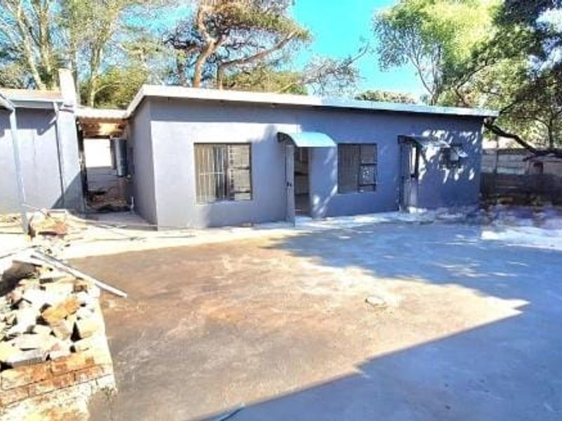 Rear exterior view of the property featuring a concrete patio area, metal roofing structure, and surrounding garden space with mature trees.