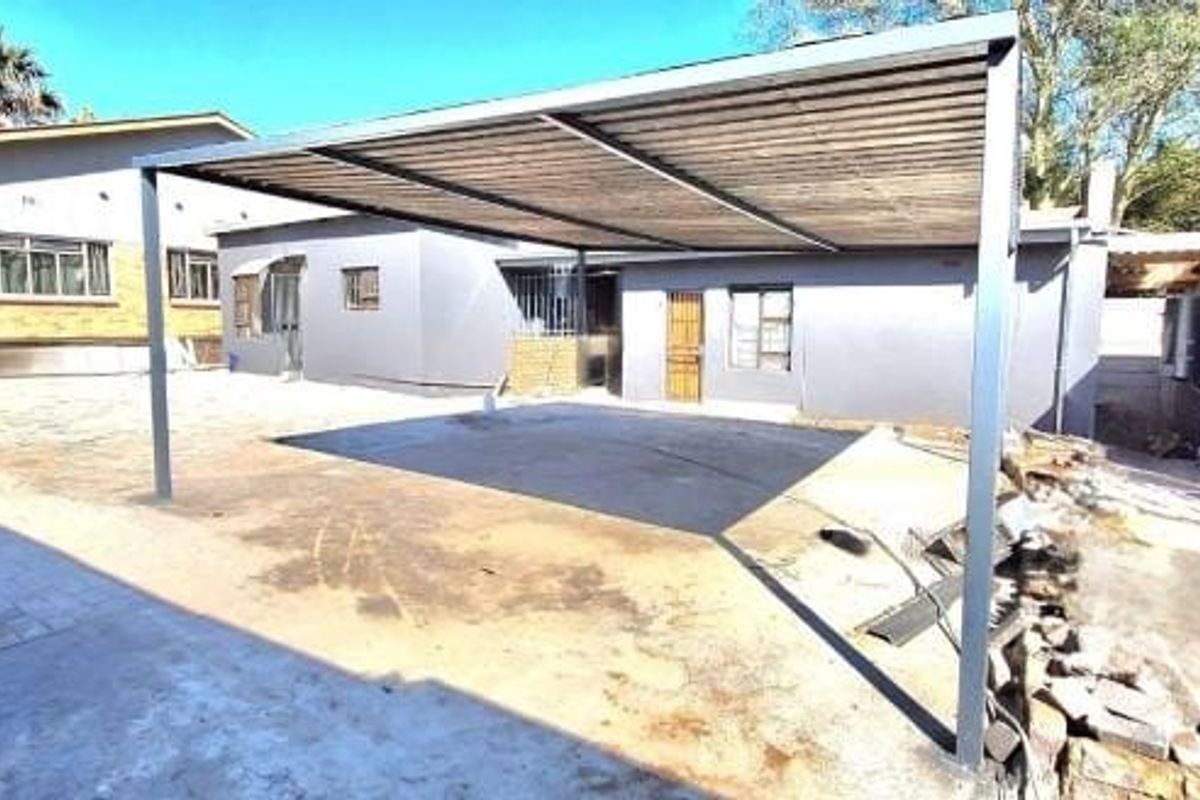 Rear exterior view featuring a metal carport structure over a paved driveway area with adjacent brick and rendered building facades.
