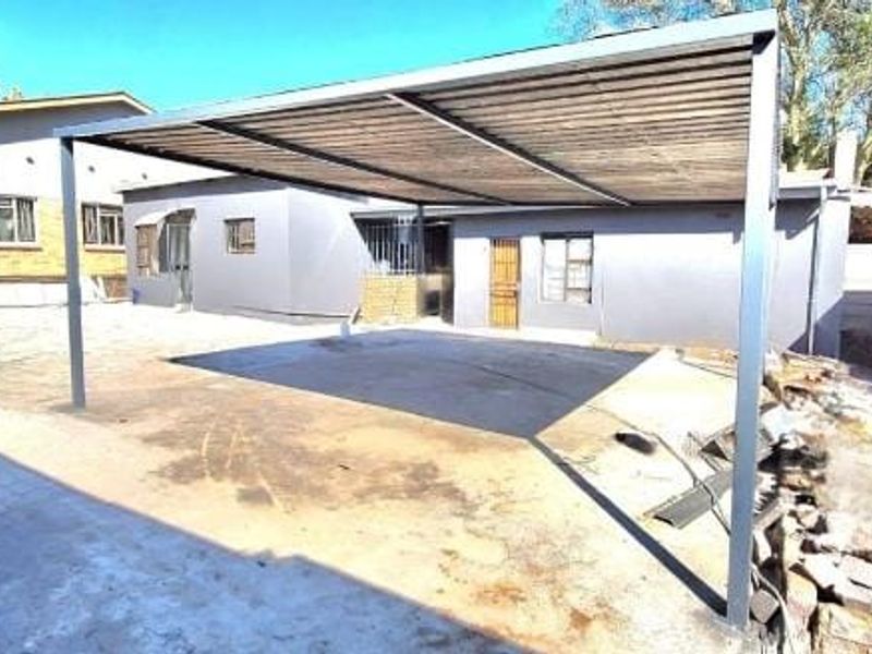 Rear exterior view featuring a metal carport structure over a paved driveway area with adjacent brick and rendered building facades.