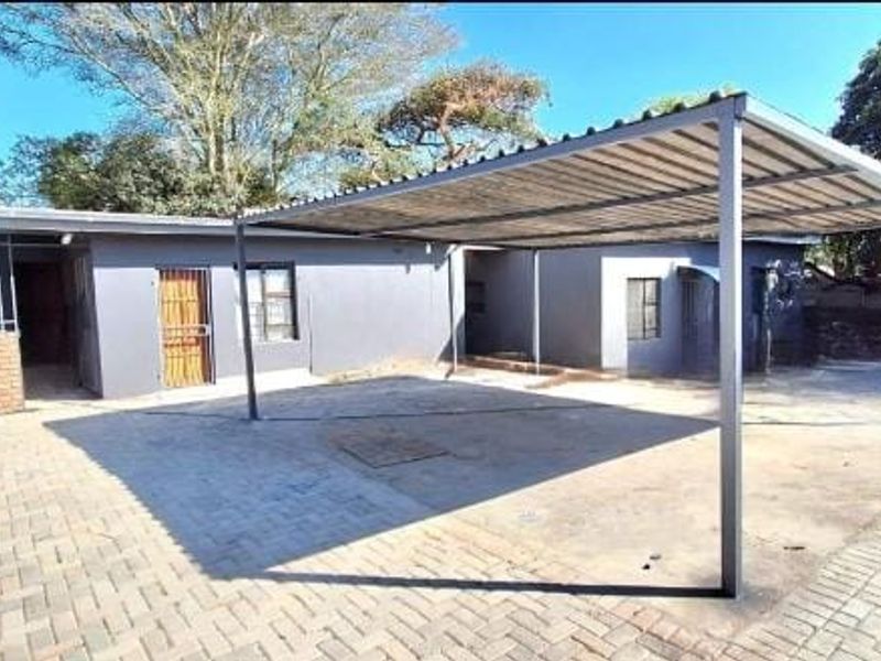 Front exterior view featuring a paved driveway, a metal carport structure, and secure access points with security gates and bars.