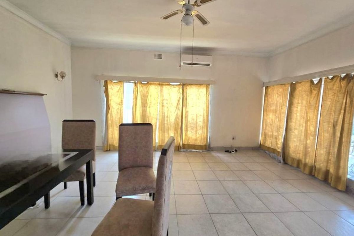 Spacious living area featuring tiled flooring, a ceiling fan, and a wall-mounted air conditioning unit with large sliding doors providing natural light.