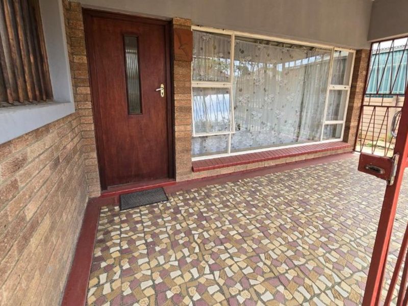 A covered patio area featuring brick walls, tiled flooring, and a secure metal gate entrance.