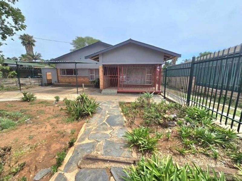 Front view of a single-story house featuring a paved walkway, covered patio area, and metal security fencing.