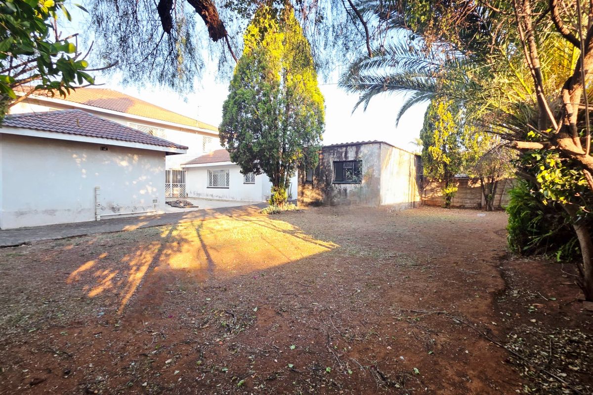 A view of the rear garden area featuring a paved patio, established trees, and the rear elevation of the house with tiled roofing.
