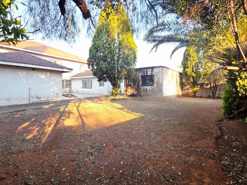 A view of the rear garden area featuring a paved patio, established trees, and the rear elevation of the house with tiled roofing.