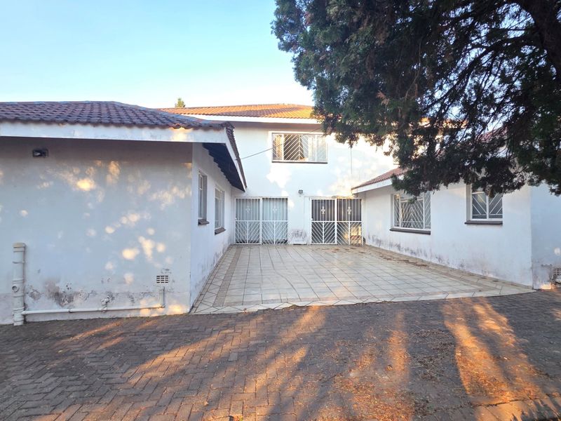Rear view of the property featuring a paved driveway, a tiled patio area, and security-fitted windows and doors.