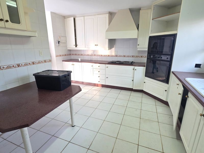A spacious kitchen featuring white cabinetry, built-in oven, hob, and tiled finishes, offering a functional layout ready for modernization and cosmetic updates.