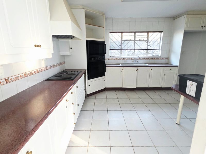 A dated kitchen featuring white cabinetry, laminate countertops, built-in oven, electric hob, and tiled flooring, offering a blank canvas for renovation.