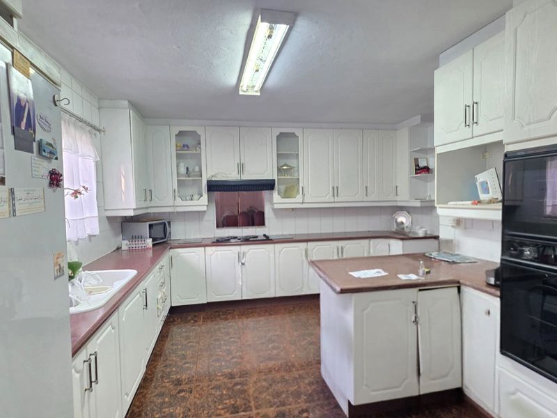 A functional kitchen featuring white built-in cabinetry, laminate countertops, integrated oven, and hob, offering a classic layout with ample storage space.